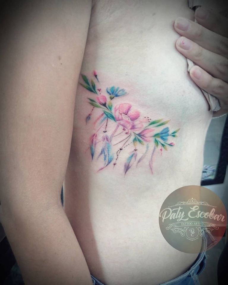 Flores colores debajo del pecho tatuaje realizado por Paty Escobar